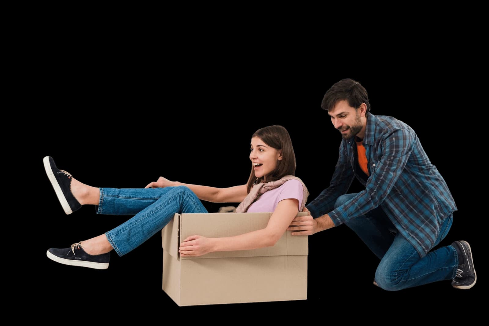 Two people happily moving — woman sitting in a cardboard box being pushed by a man, both smiling